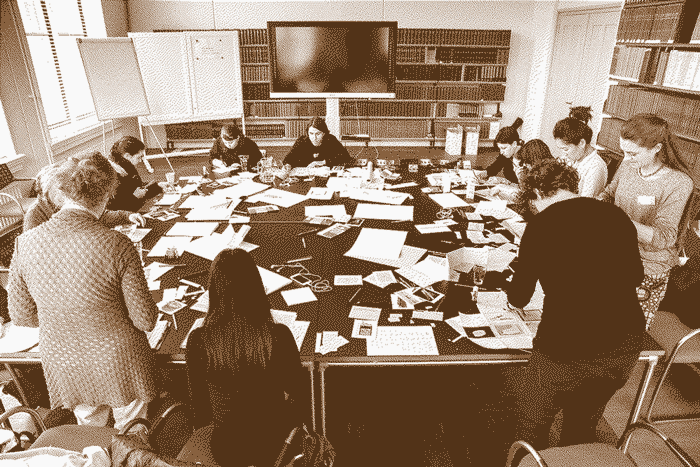 A large table covered in papers and materials with the participants and workshop givers surrounding it.